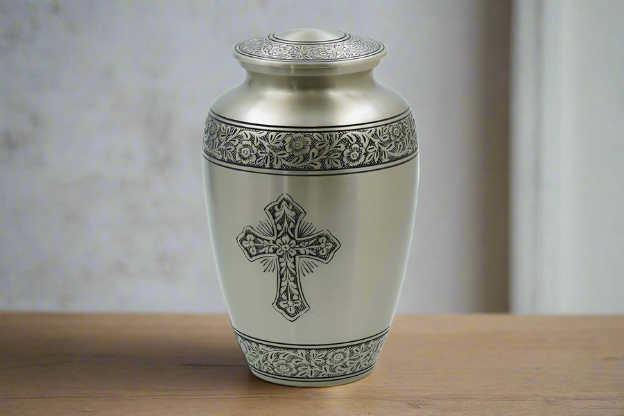 Brass metal urn with a cross displayed on a wooden countertop